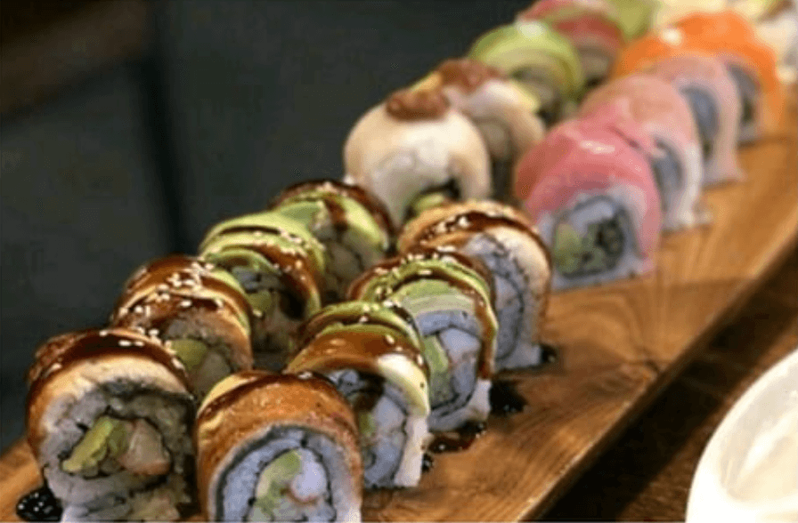 Two vertical lines of sushi topped with avocado, raw fish, and drizzles of sauce.
